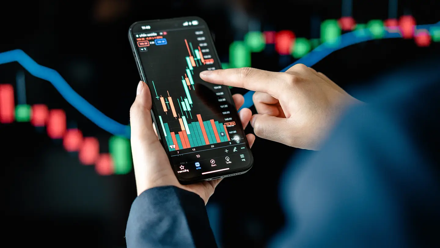 Persona usando un teléfono inteligente para analizar gráficos financieros, con datos de inversión en panta
