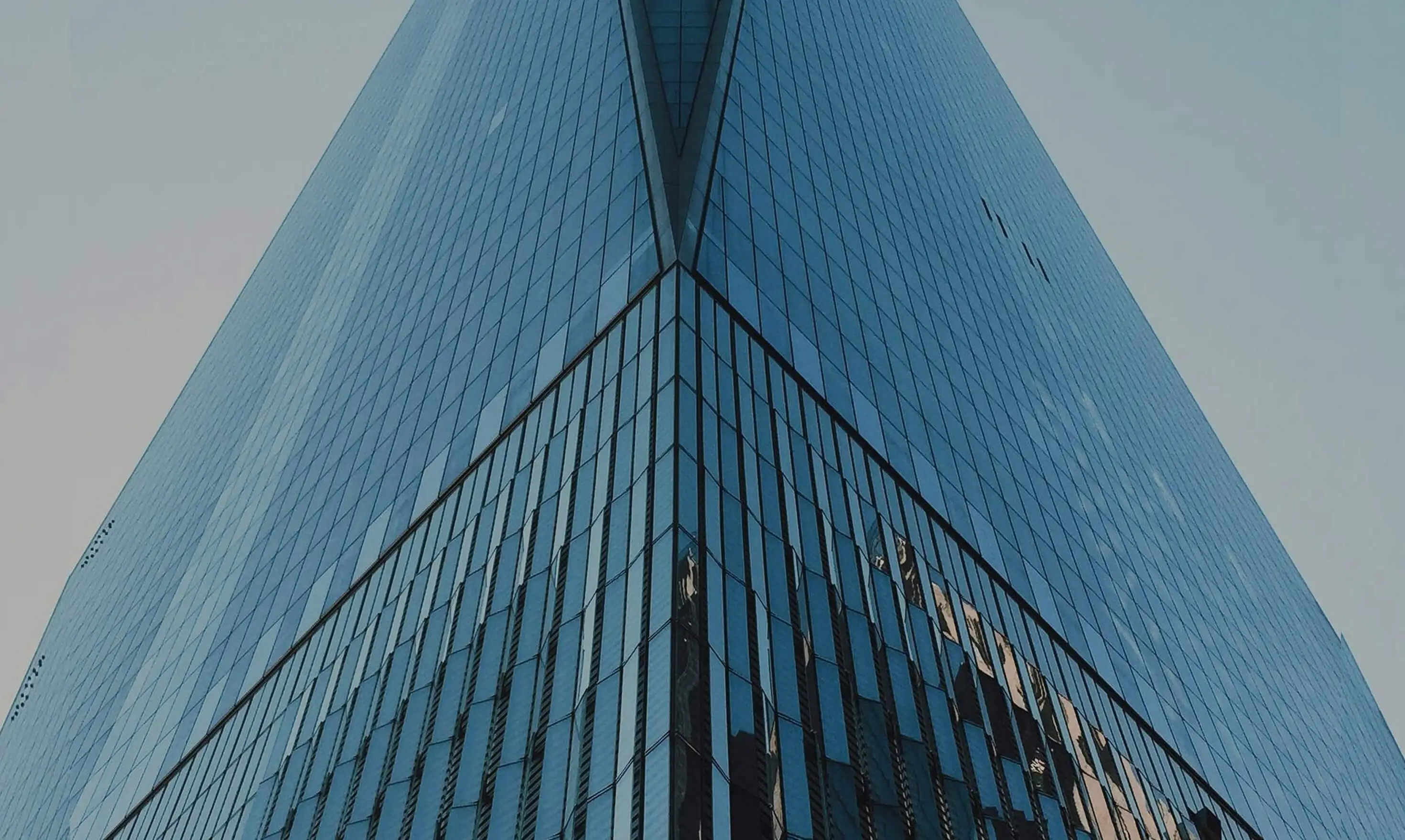 Edificio moderno de cristal visto desde un ángulo inferior, con fachada reflectante y líneas simétricas.
